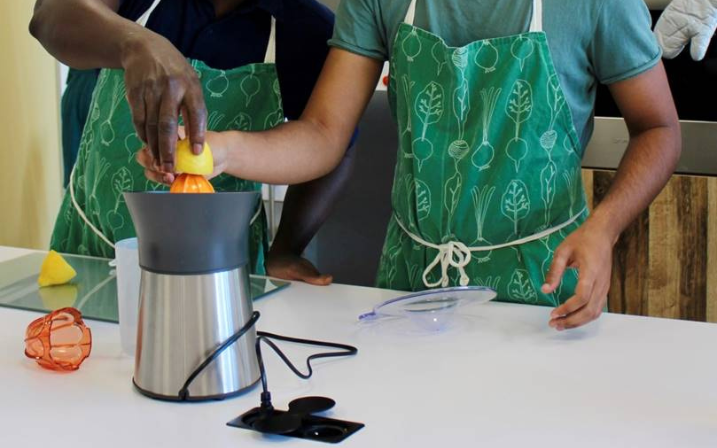 Deux personnes portant un tablier de cuisine sont debout devant un plan de travail et pressent un citron à l'aide d'un presse-agrume visible en premier plan.