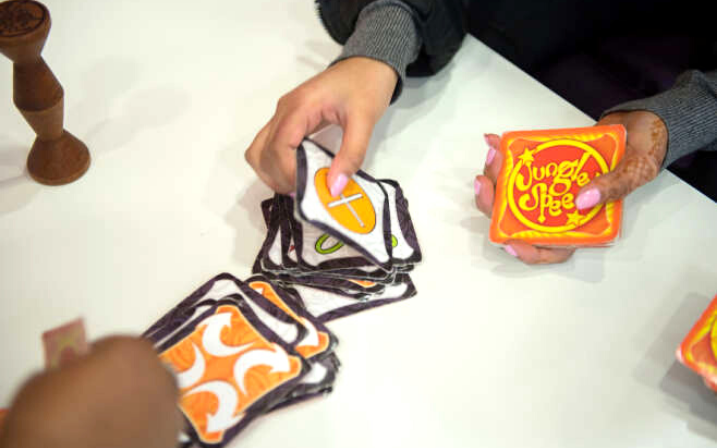 Une personne distribue des cartes tandis qu'une autre en attrappe sur la table. La photo montre seulement les mains et le tas de cartes sur la table blanche.